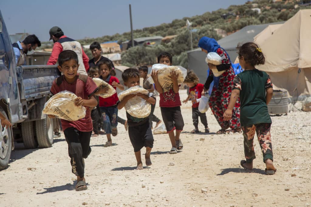 Glückliche Kinder rennen mit Tüten voll frischem Brot, das von humanitären Helfern in einem Zeltlager verteilt wurde.