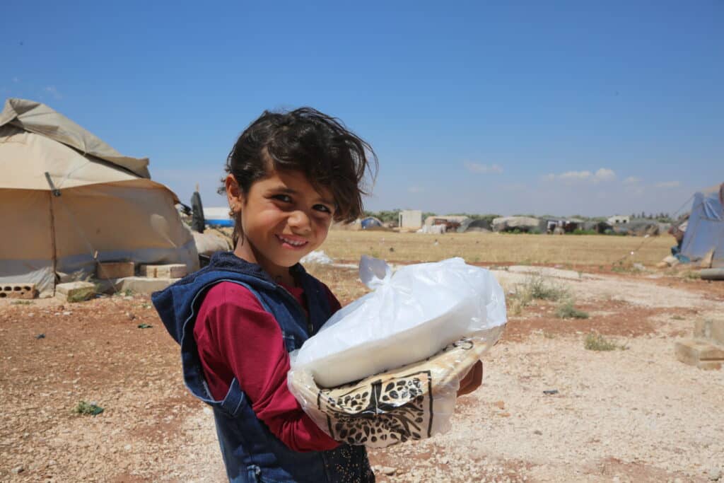 A smiling young girl holding a package of fresh bread in a refugee camp during a food distribution.