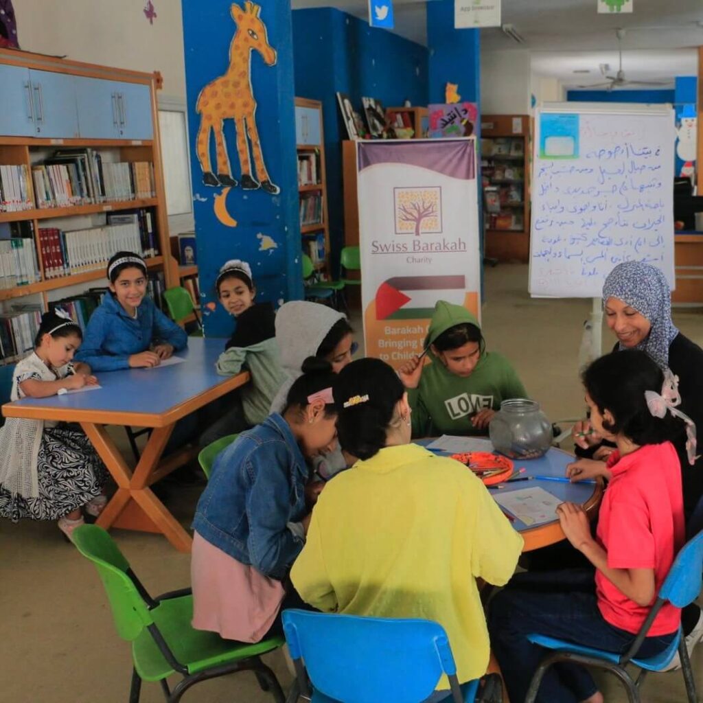 Un'insegnante supporta i bambini durante una lezione della Barakah Charity. Le tue donazioni per Gaza offrono un aiuto diretto sul campo.