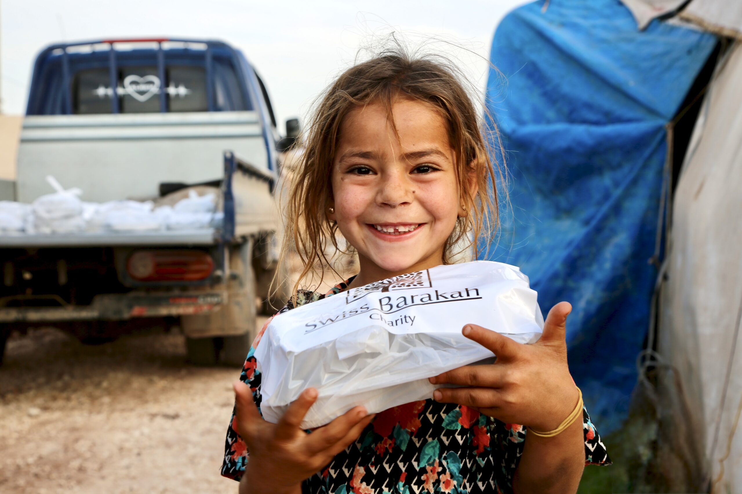 Smiling girl holding a warm Iftar meal during a charity food distribution project.