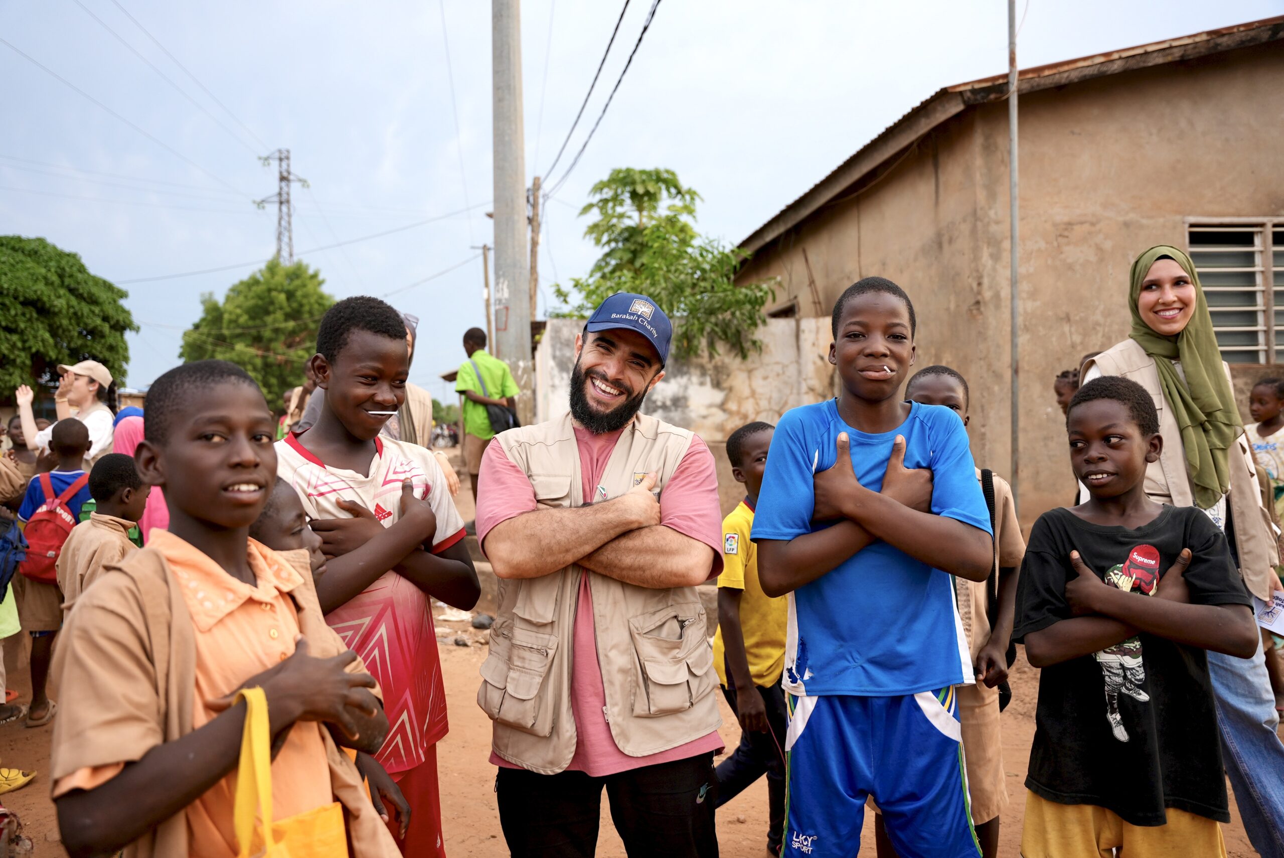Volontari di Barakah Charity sorridenti insieme ai bambini locali durante una missione di aiuto sul campo.
