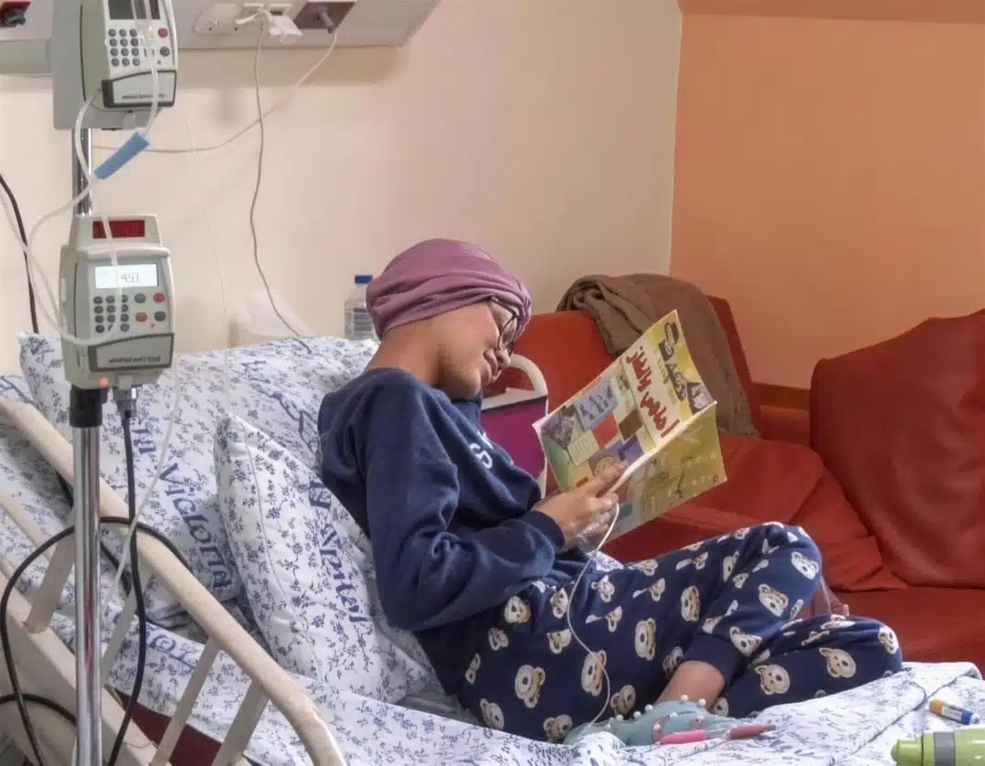 Ein Kind liest ein Buch in einem Krankenhausbett mit Infusion – medizinische Versorgung für Patientinnen und Patienten.