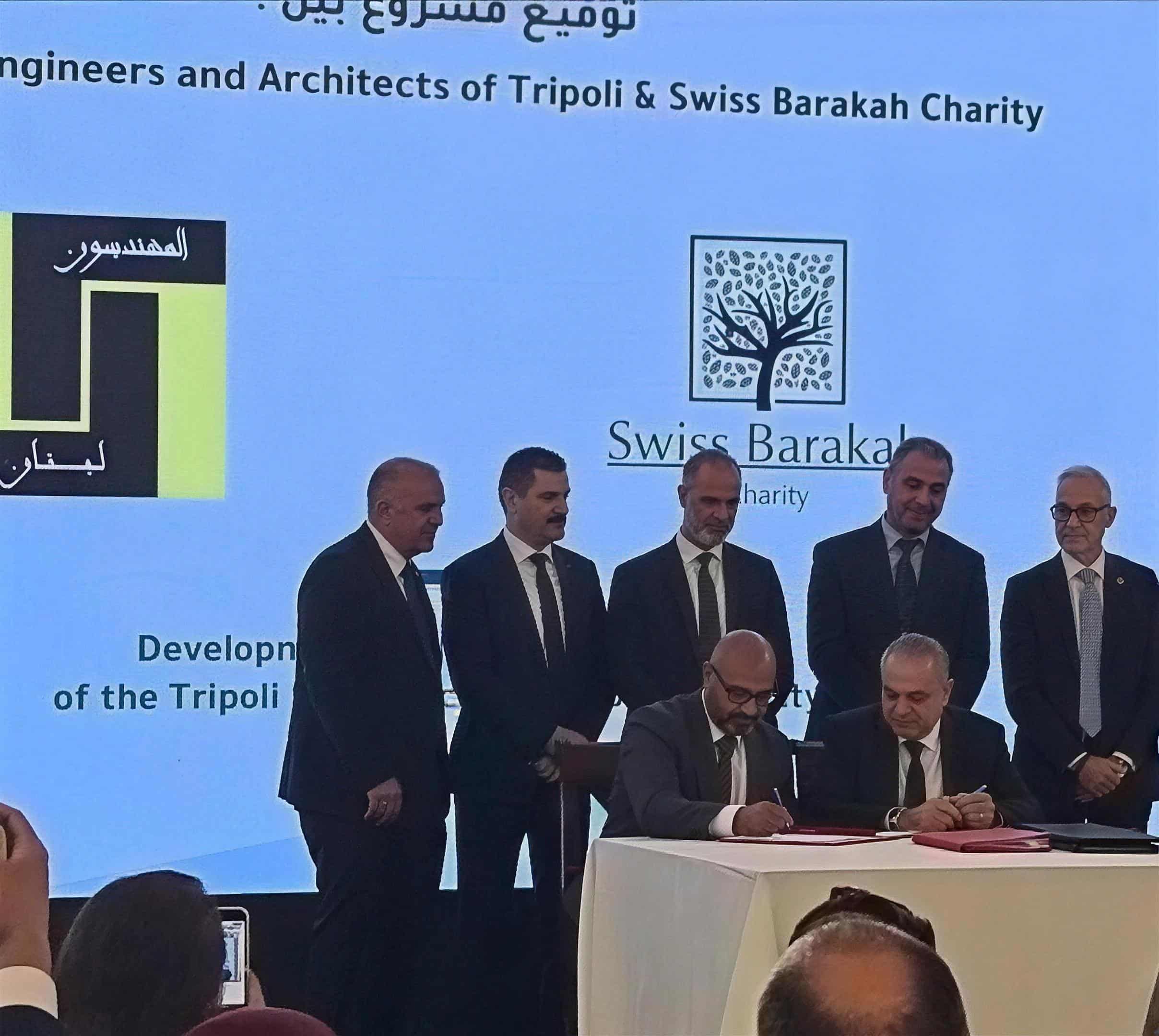 Unterzeichnung der Vereinbarung zwischen der Ingenieur- und Architektenkammer Tripoli und Swiss Barakah Charity, im Hintergrund die Logos beider Organisationen